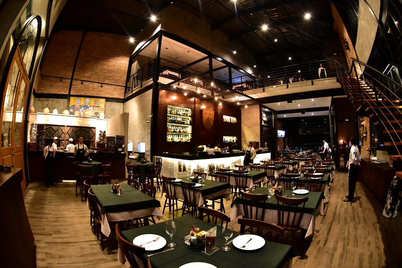 Foto real do interior da Troina, com bar, mesas, mezanino e escadaria